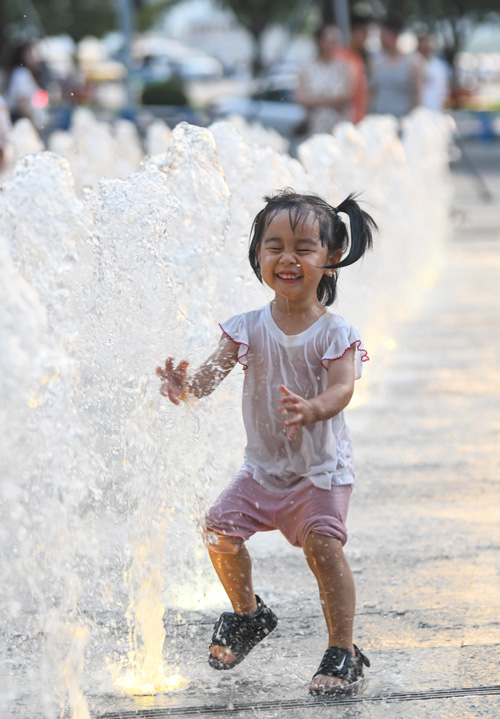 7月10日，孩子們?cè)谀蠟I路噴泉下戲水玩耍享受清涼。郭旭攝